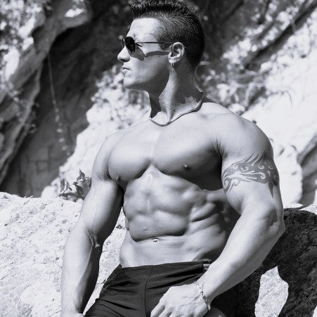 A nice muscular man with sunglasses sitting on a rock